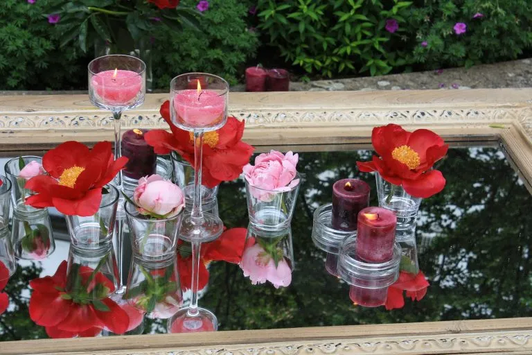 Tischdekoration mit Blüten und Kerzen auf einem Spiegel